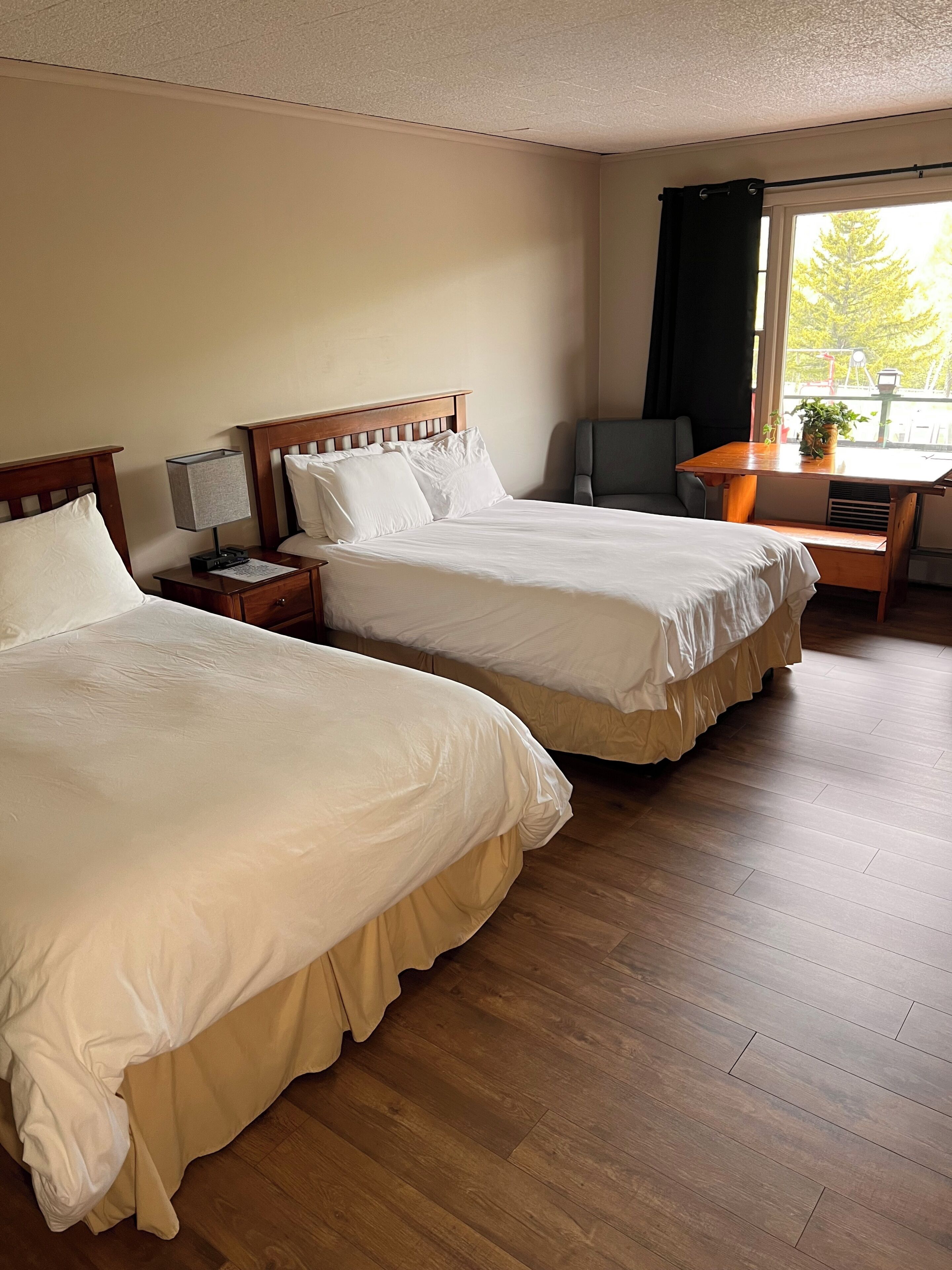 Habitación de hotel con dos camas, un escritorio y ventana con vista a árboles.