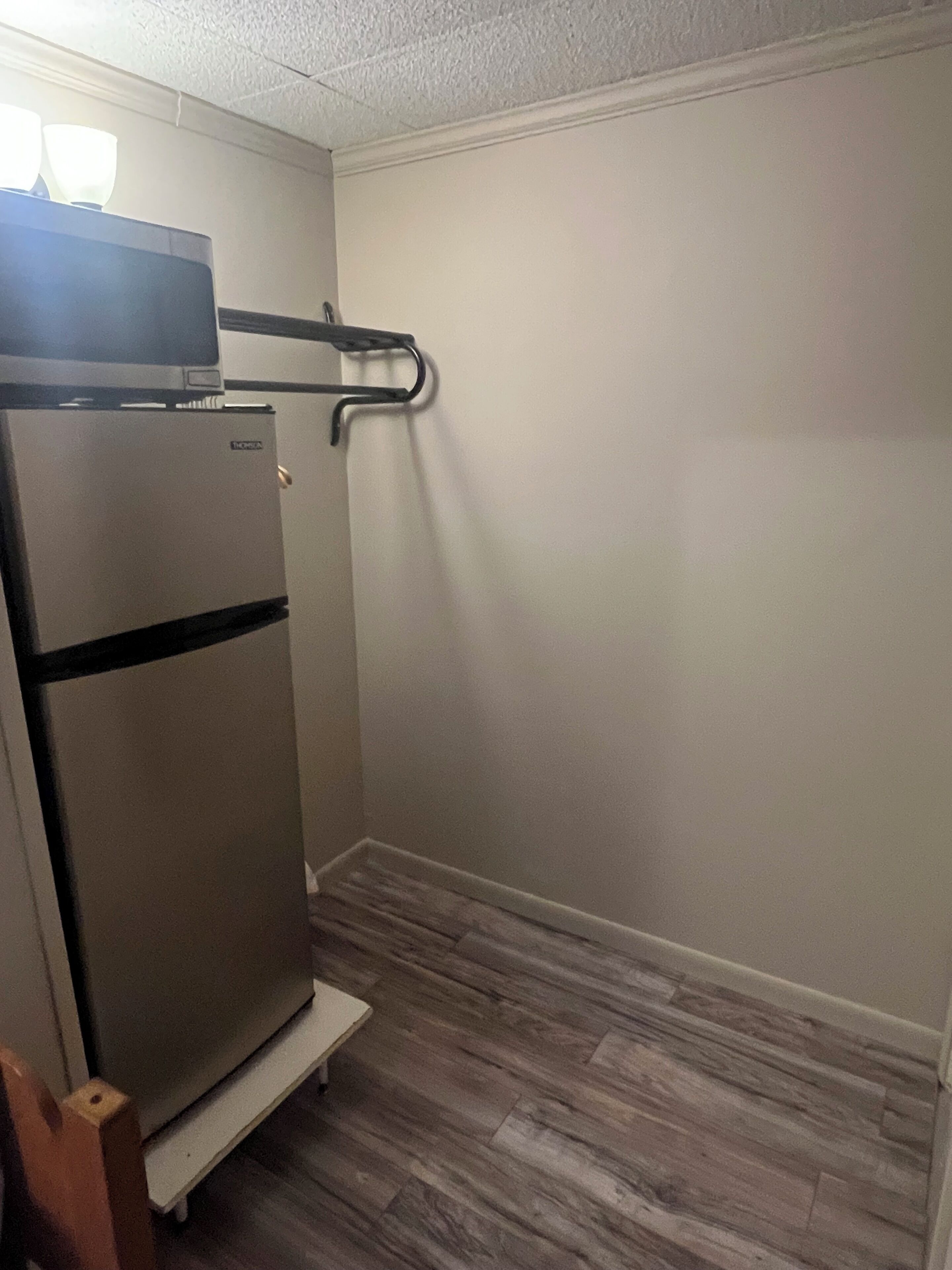 Eine kleine Küchenzeile mit integriertem Kühlschrank und Mikrowelle, Holzboden und weißer Wand.