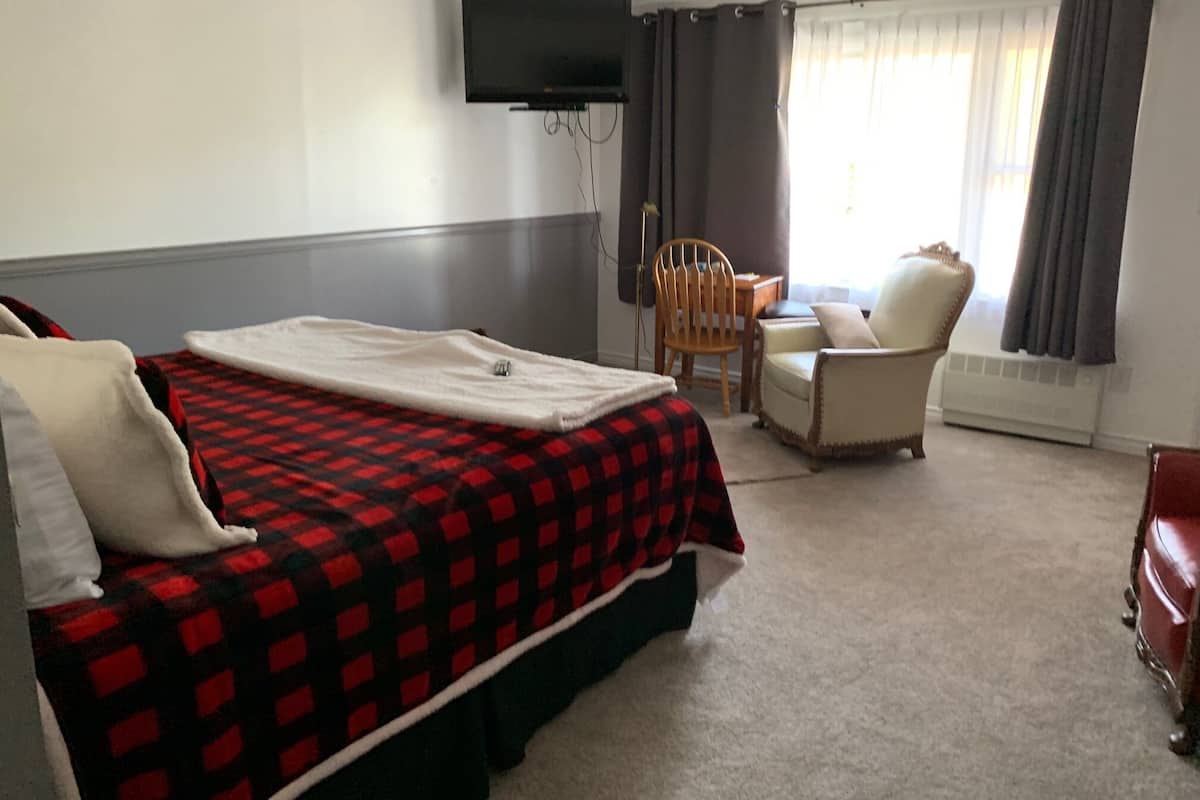 A hotel room with a bed, a chair, a table, and a TV mounted on the wall.