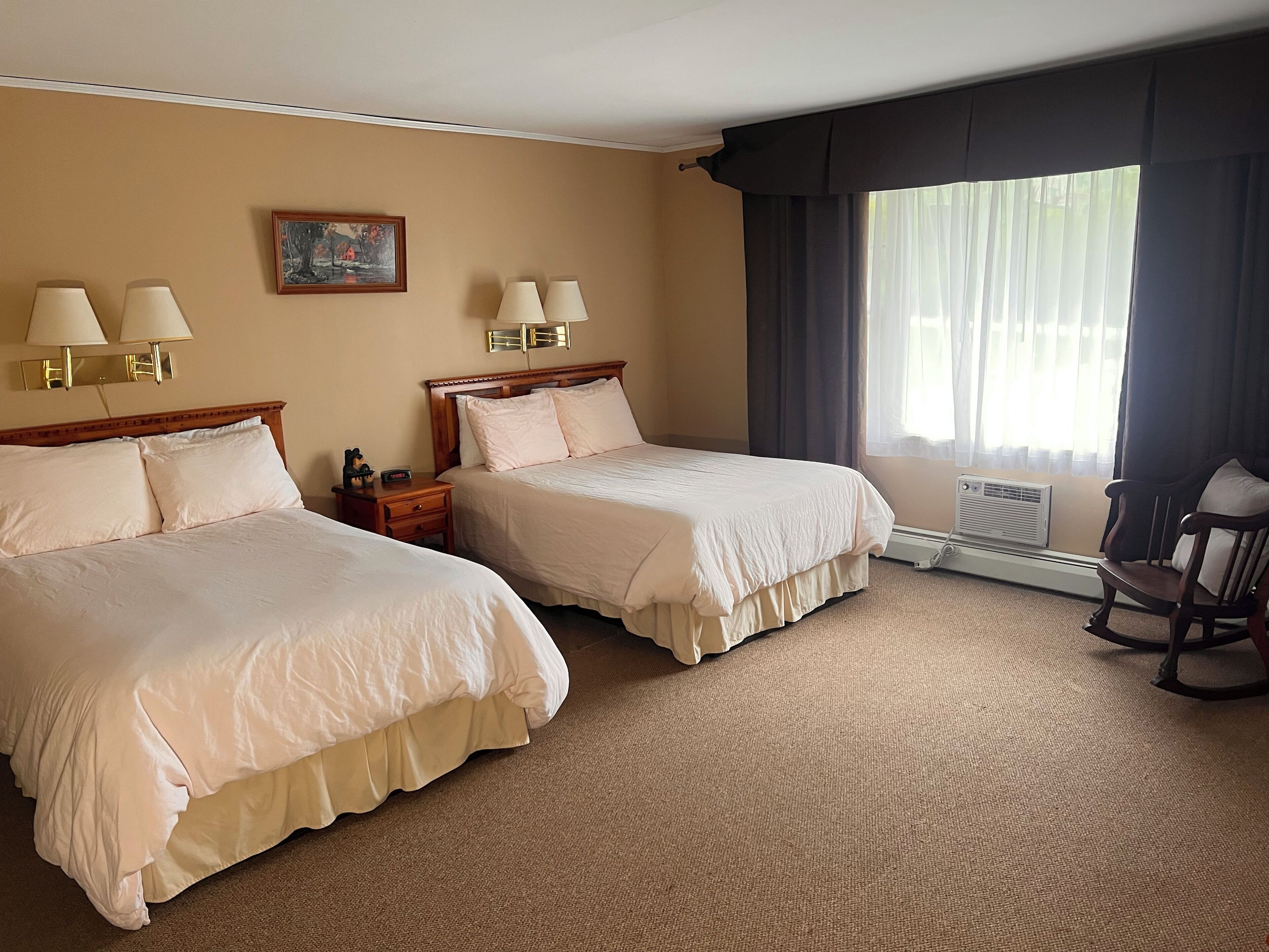 Habitación de hotel con dos camas, una mesita de noche, una silla, un cuadro y una ventana con cortinas.