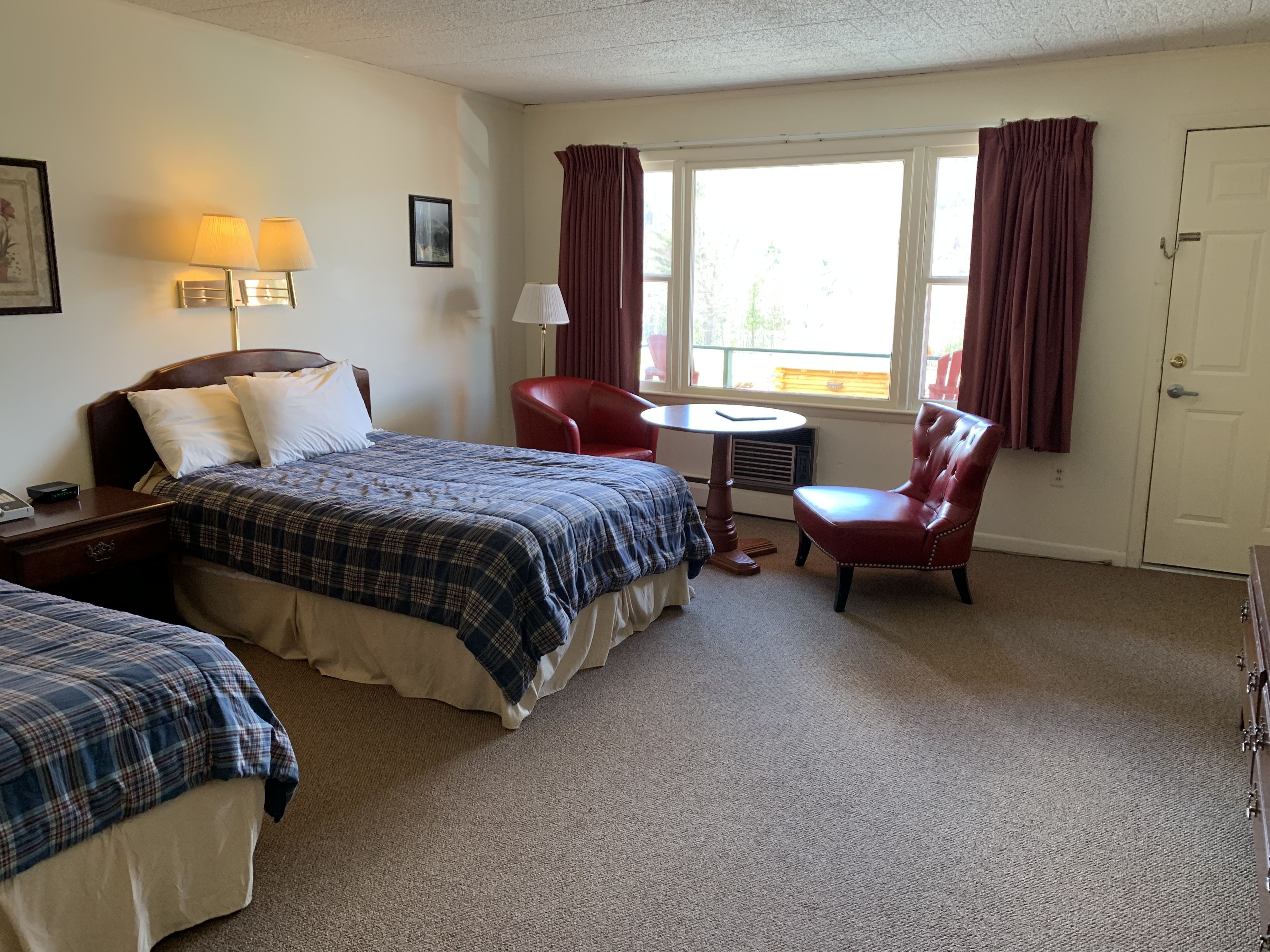 A hotel room with two beds, a desk, a chair, a table, and a window with curtains.