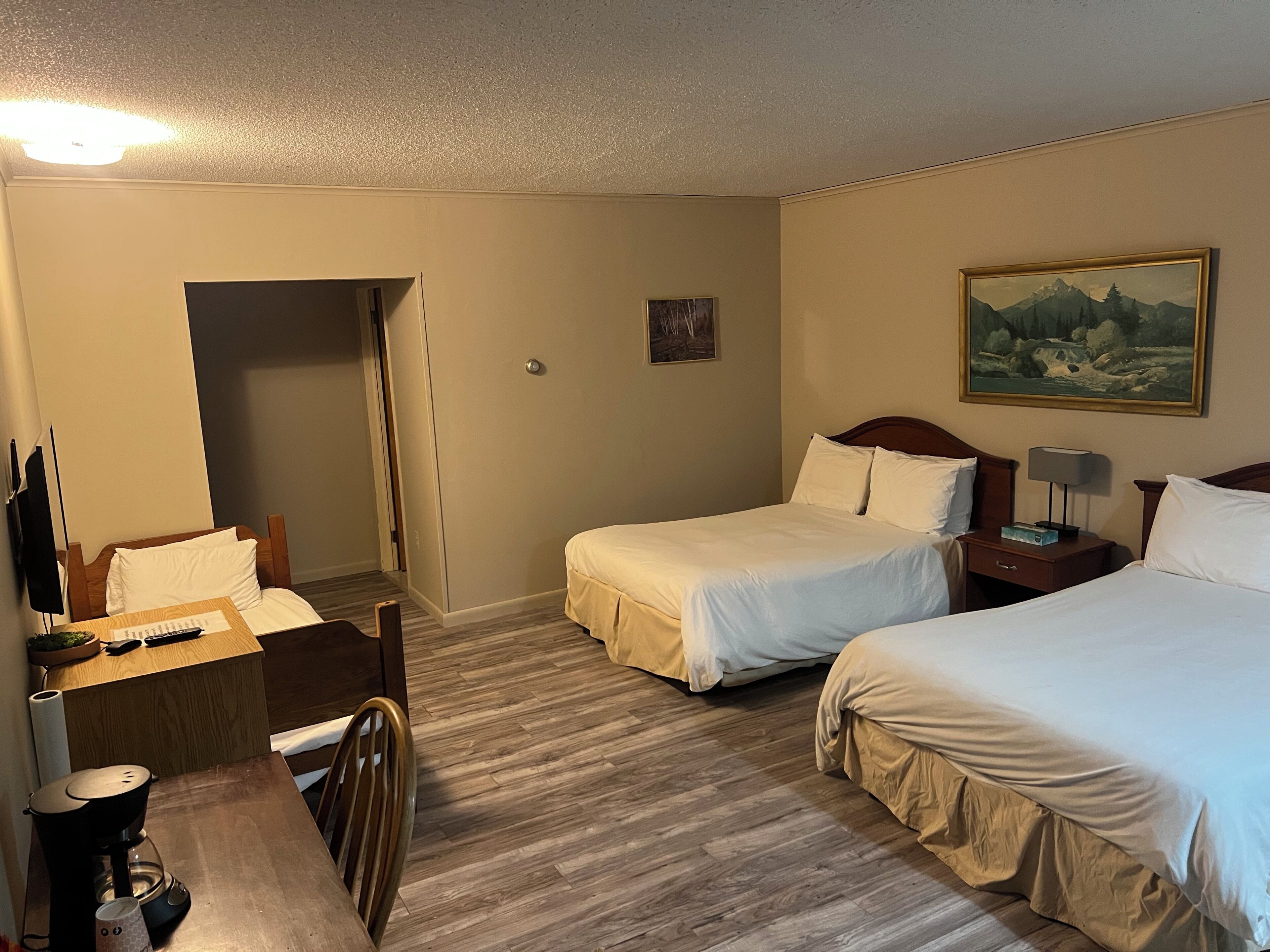 A hotel room with two beds, a desk with a chair, a coffee maker, and a painting on the wall.