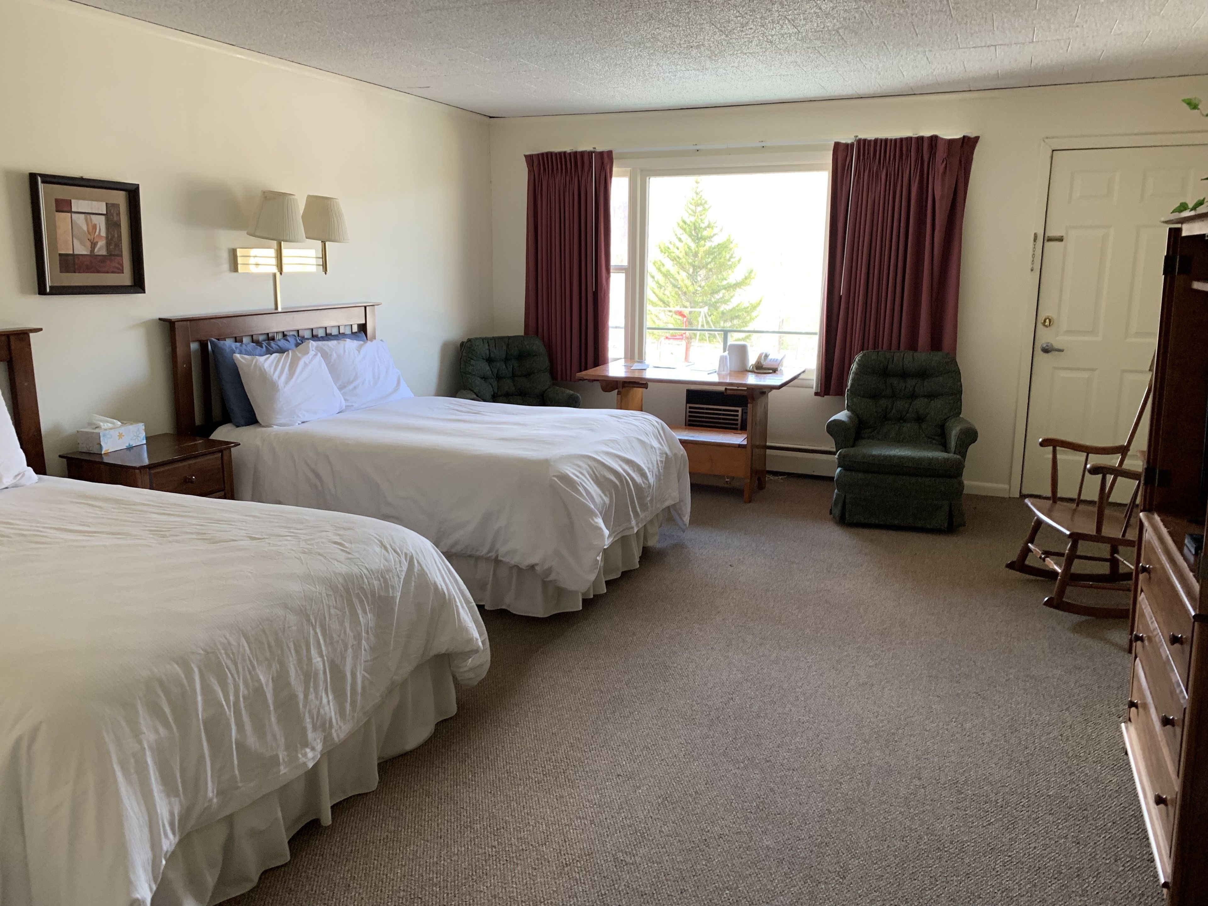 Habitación de hotel con dos camas, un escritorio, una silla y un aparador.