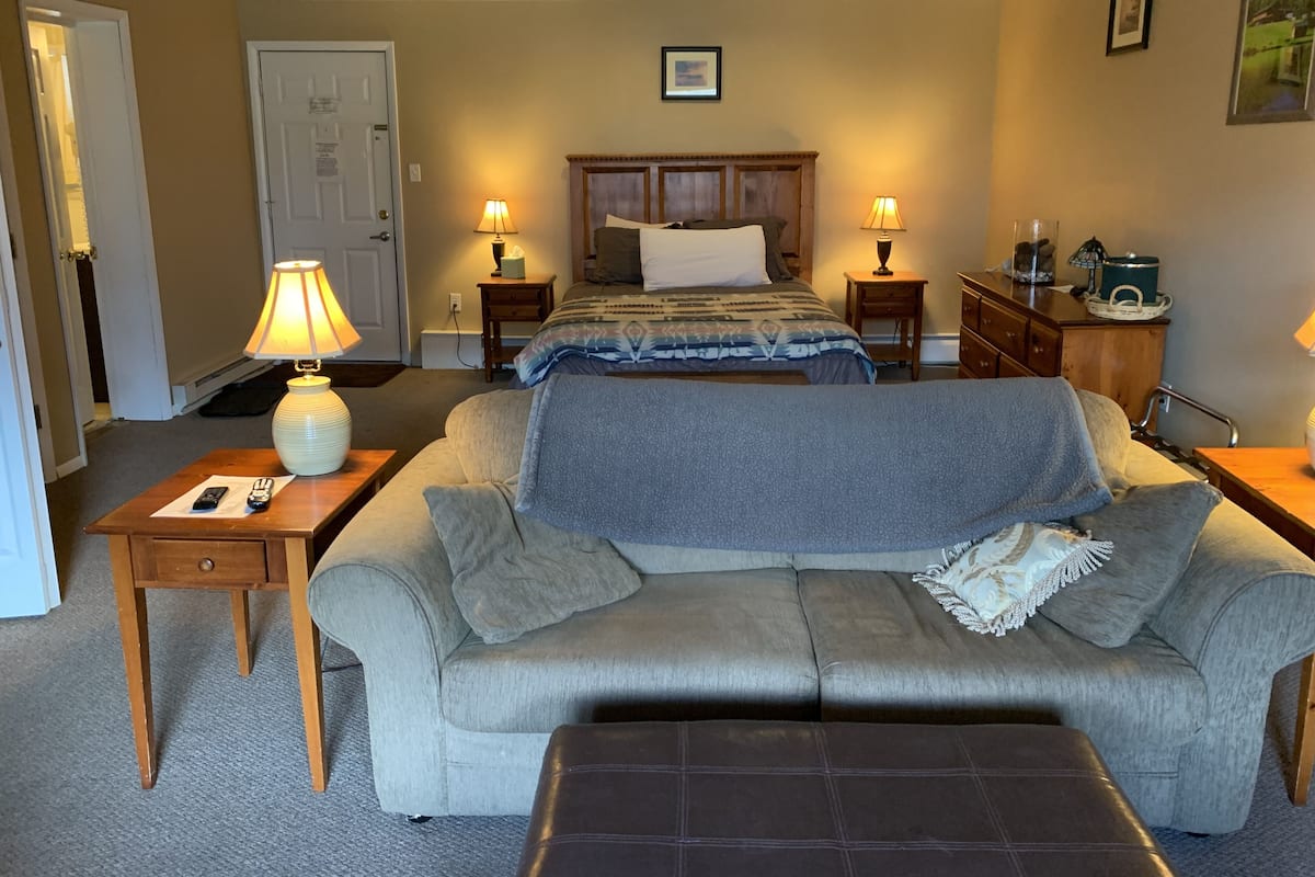 A hotel room with a bed, a sofa, a small table, and a nightstand.