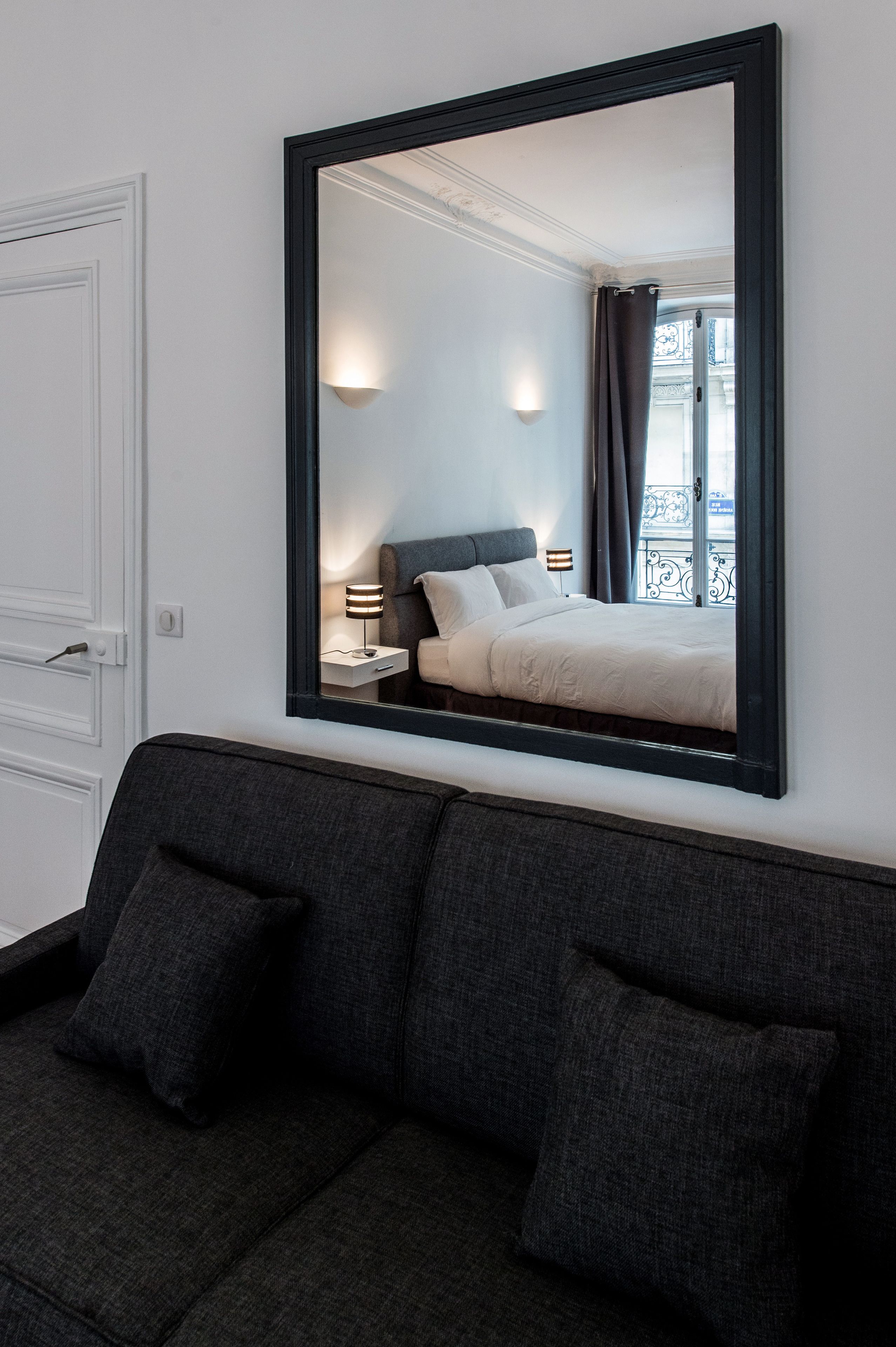 Habitación de hotel con un espejo grande que refleja una cama, mesitas de noche y un ventanal con cortinas.