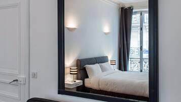 Habitación de hotel con un espejo grande que refleja una cama, mesitas de noche y un ventanal con cortinas.