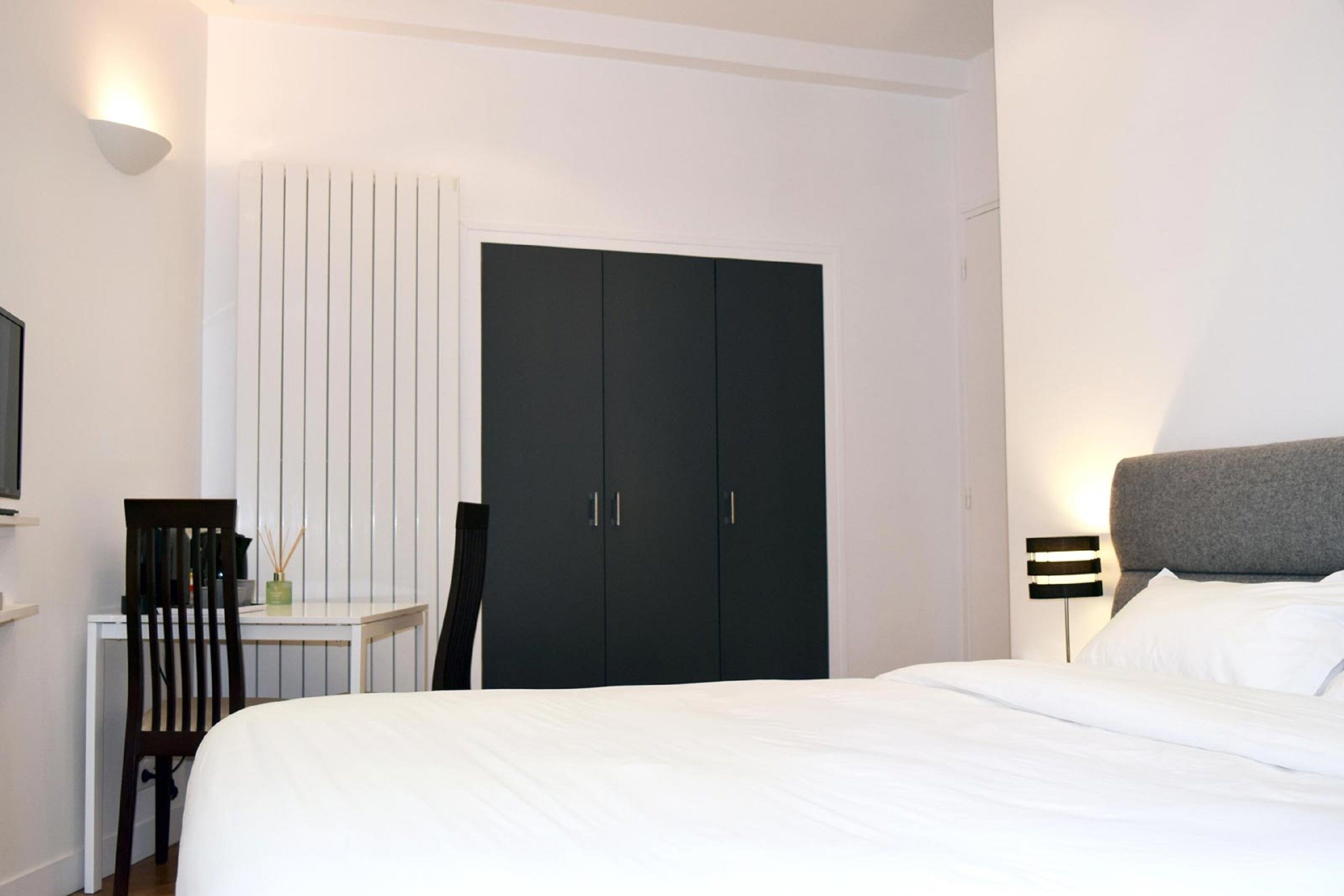 Een slaapkamer met een bed, een bureau, een stoel, een kledingkast en een nachtkastje met een lamp.