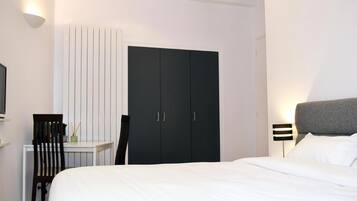 Een slaapkamer met een bed, een bureau, een stoel, een kledingkast en een nachtkastje met een lamp.