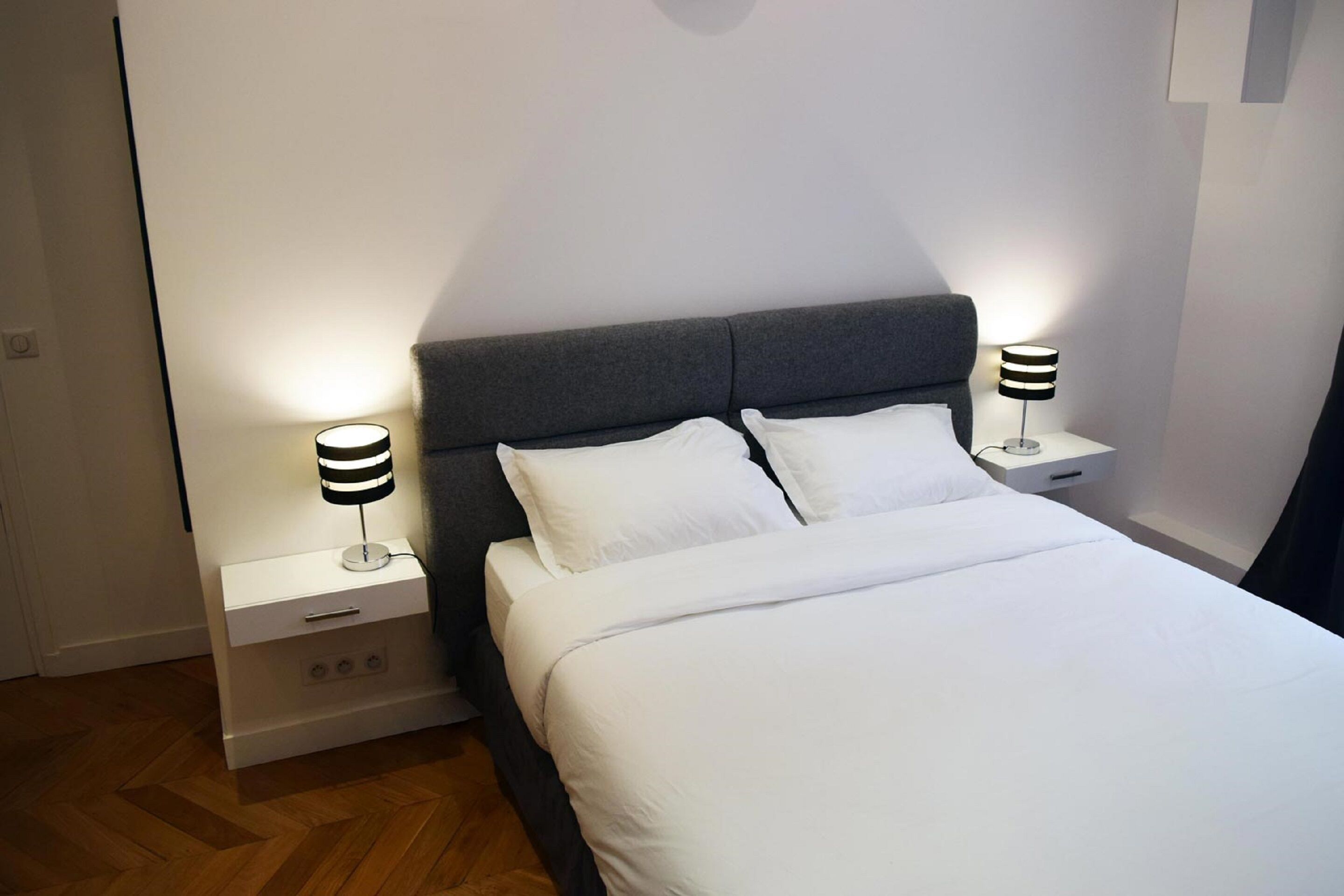 Un lit bien fait, avec du linge de lit blanc et deux tables de chevet avec des lampes.