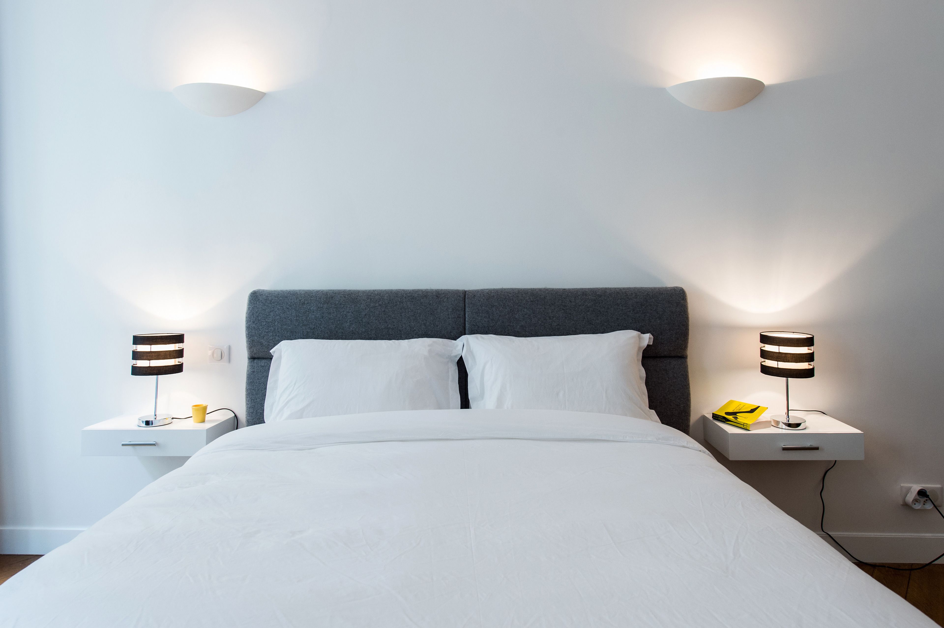A neatly made bed with white linens, two bedside tables with lamps, and a grey headboard.