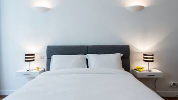 A neatly made bed with white linens, two bedside tables with lamps, and a grey headboard.
