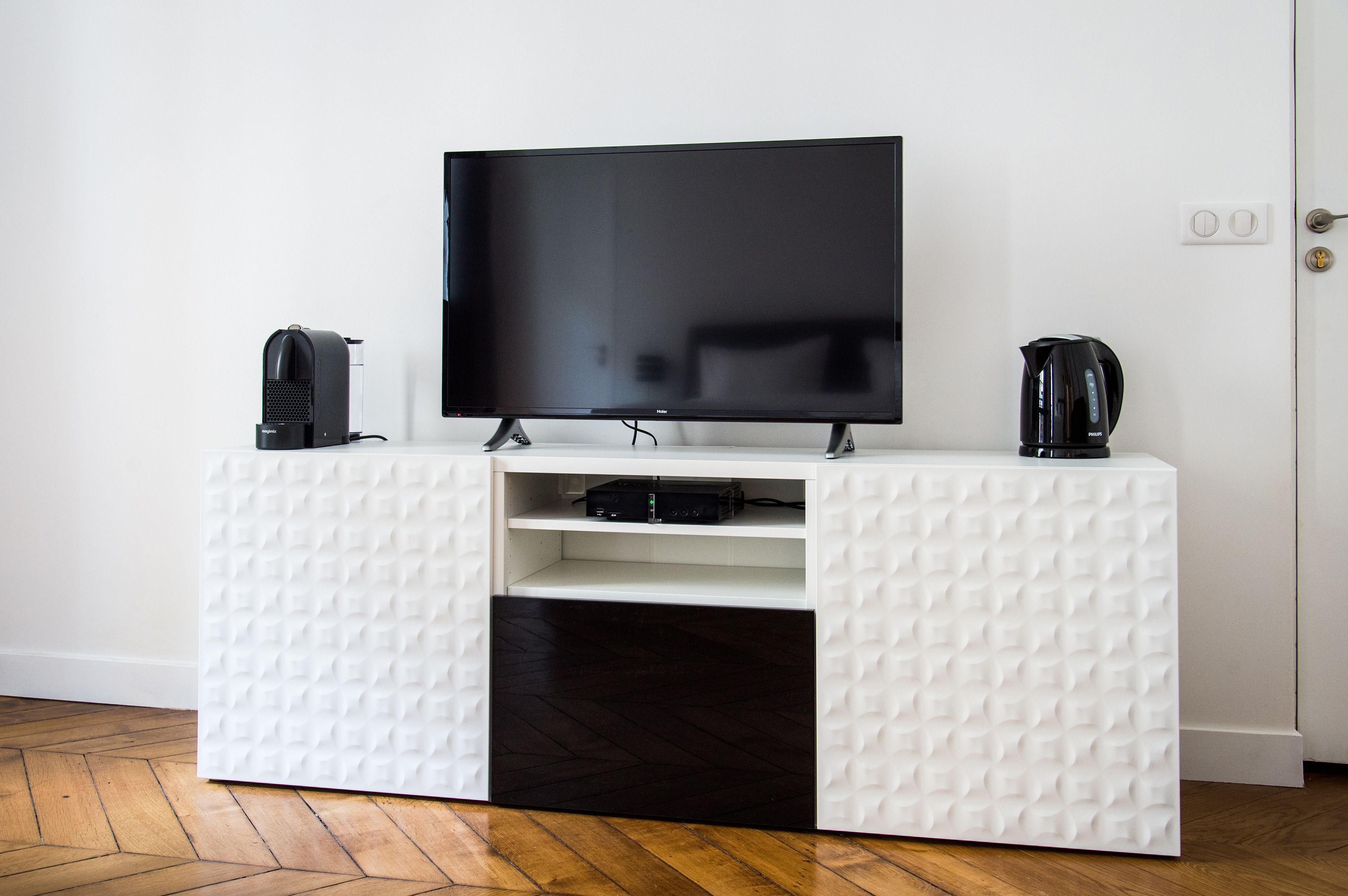 A white entertainment unit with a flat-screen TV, a coffee maker, and a speaker.
