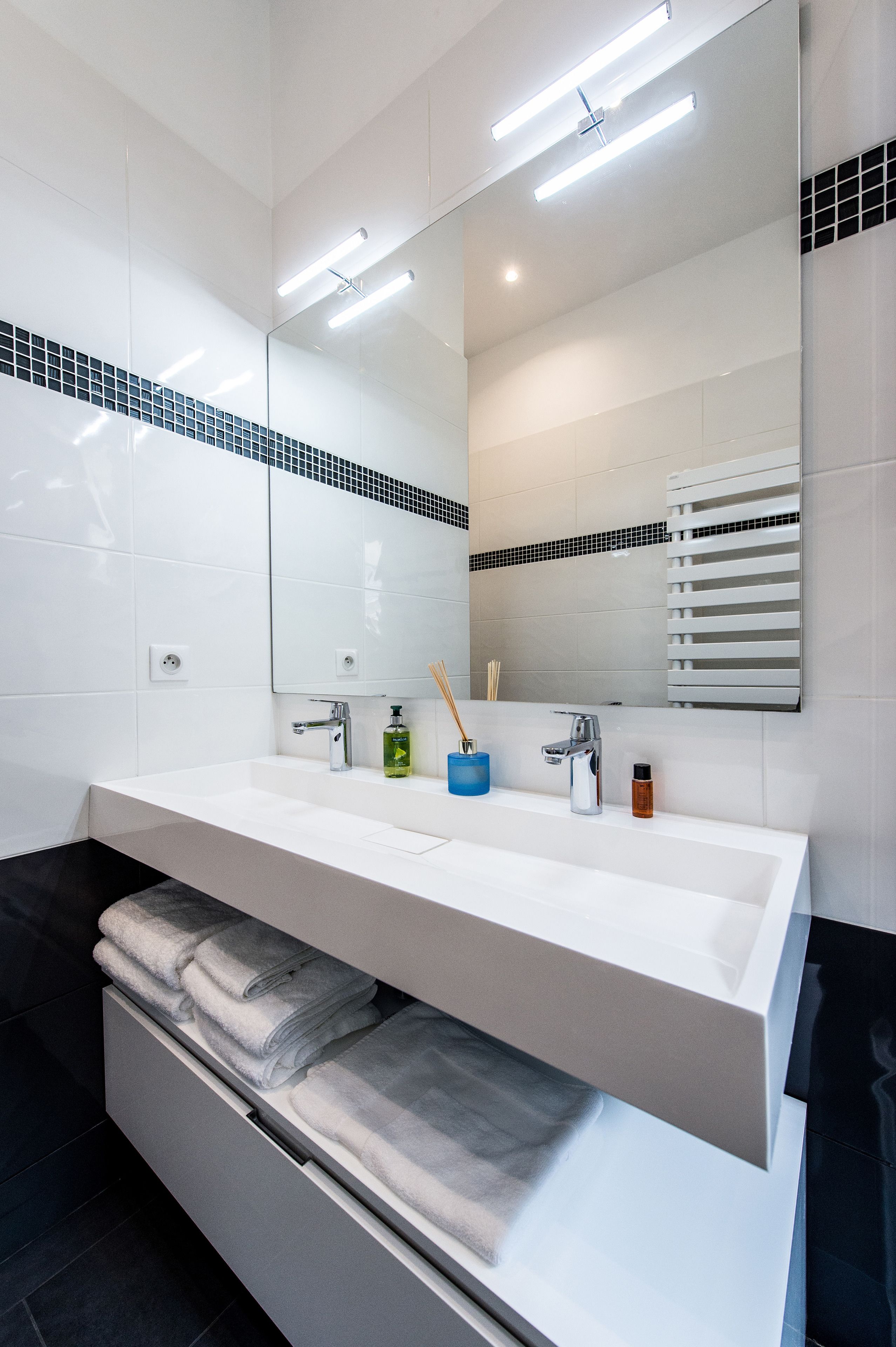 A modern bathroom with a white sink, mirror, and towel storage.