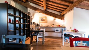 A cozy kitchen with wooden beams, a dining area with blue and red chairs, and a bookshelf filled with various items. - L'Albero di Gameli (Chiusi)