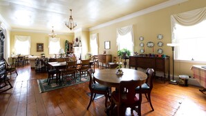 A spacious dining area with a wooden table and chairs, a chandelier, and a large window with curtains. - B&B at Oliver Phelps (Canandaigua)
