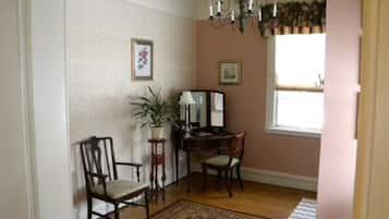 A dining area with a wooden table, two chairs, a chandelier, and a window with curtains.