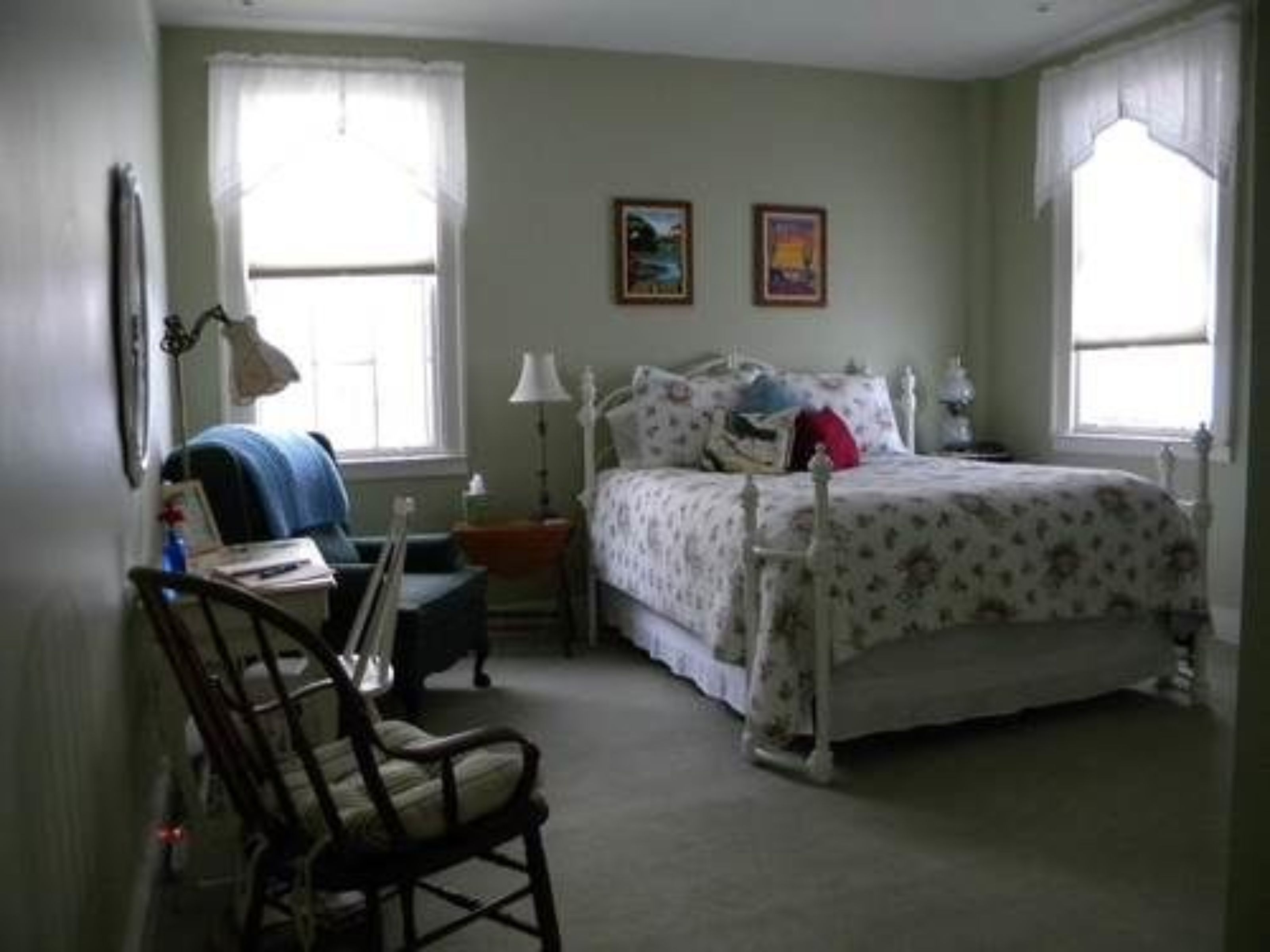 A bedroom with a bed, a chair, a desk, and two windows.