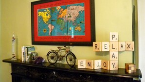 A framed world map with a red border and a quote, a Scrabble game with the word 'RELAX' spelled out, a vintage bicycle, and a small bookshelf with books and a glass container. - B&B at Oliver Phelps (Canandaigua)