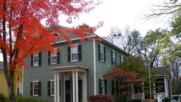 A two-story house with a front porch, green shutters, and a chimney. - B&B at Oliver Phelps (Canandaigua)
