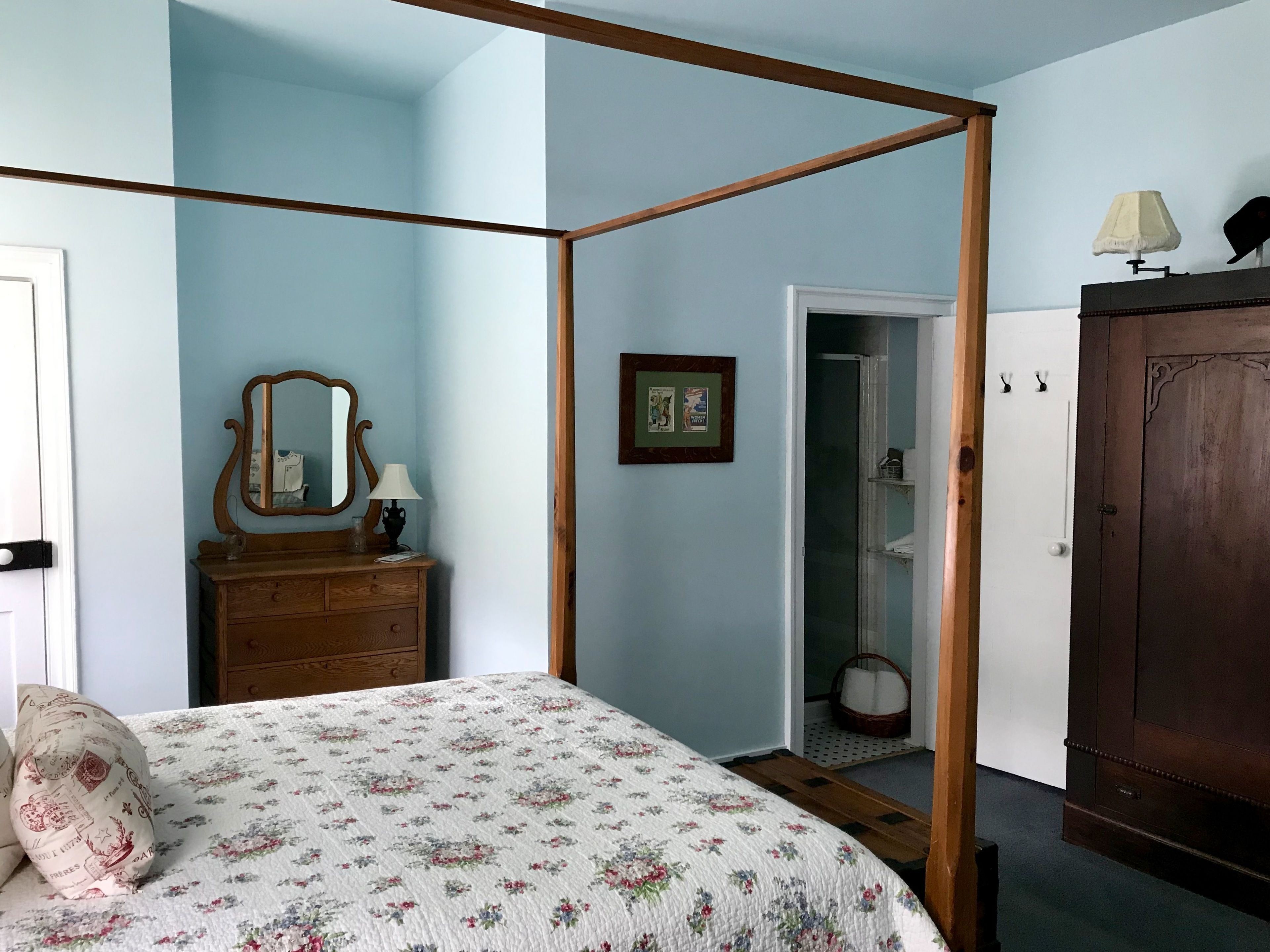 Un dormitorio con una cama con dosel, un aparador de madera, un espejo y una puerta que da al baño.