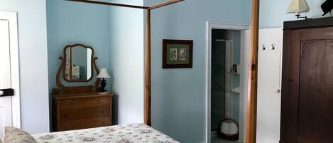 Un dormitorio con una cama con dosel, un aparador de madera, un espejo y una puerta que da al baño.