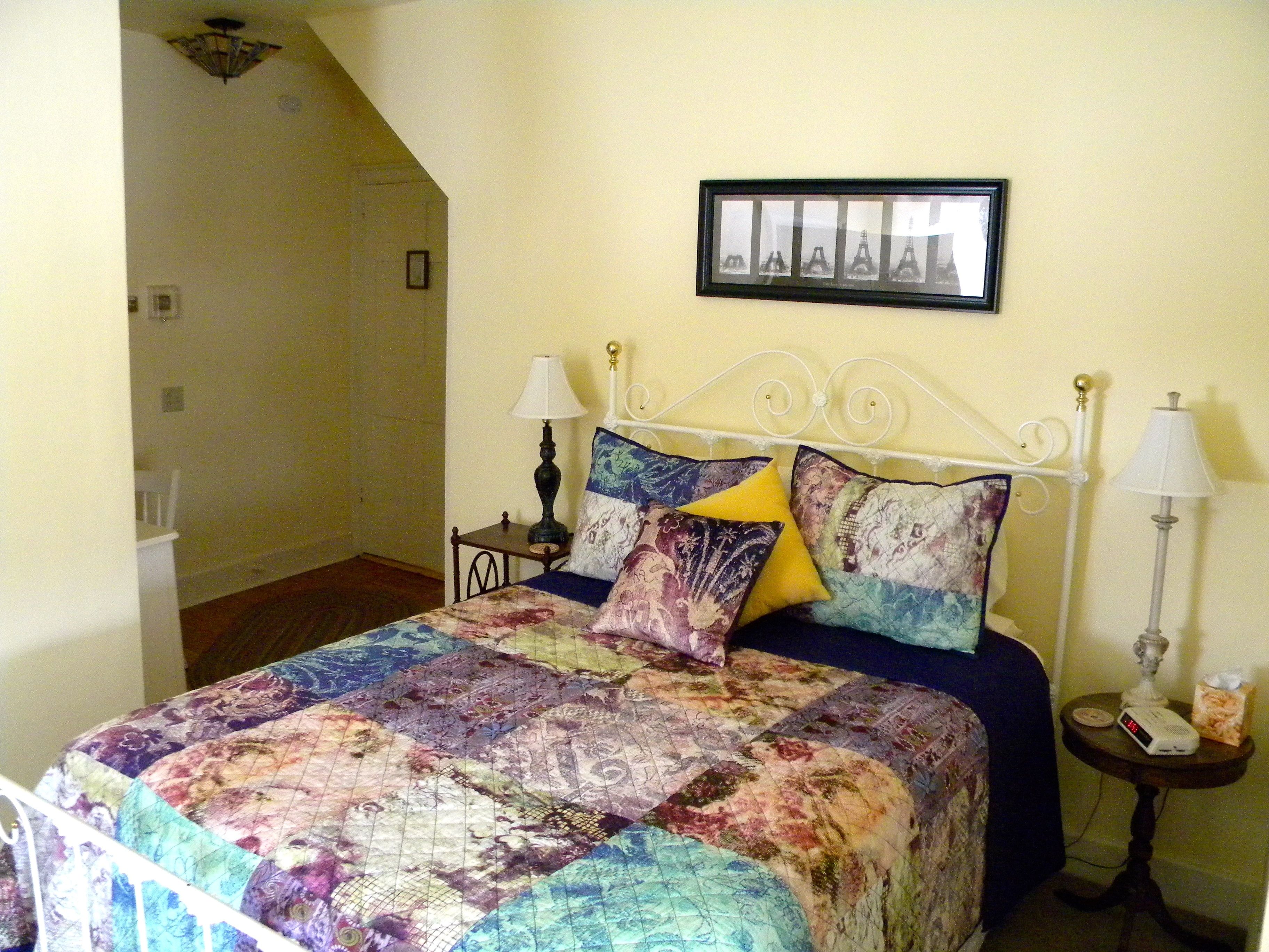 A bedroom with a bed, two bedside tables, a wall-mounted picture, and a door leading to another room.