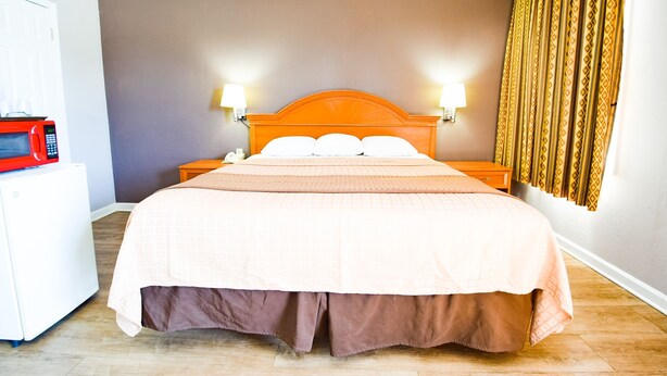 A hotel room with a bed, two bedside lamps, a microwave, and a patterned curtain. - Economy Inn Beebe (Beebe)