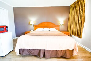 A hotel room with a bed, two bedside lamps, a microwave, and a patterned curtain. - Economy Inn Beebe (Beebe)