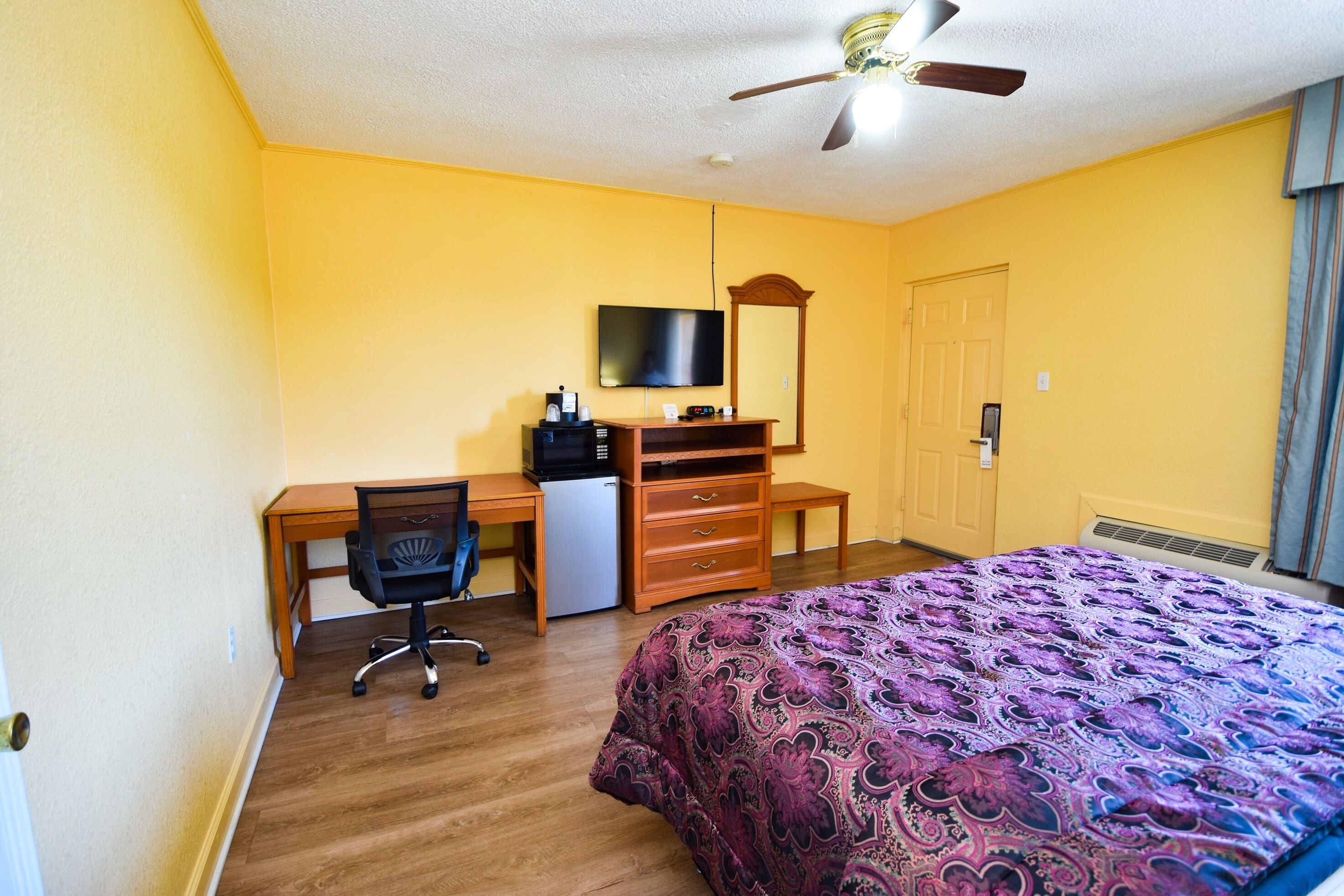 A bedroom with a bed, desk, chair, television, and a ceiling fan.