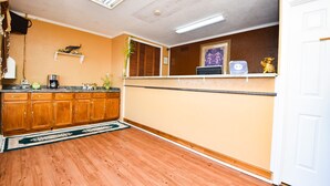 A kitchen with wooden cabinets, a countertop with appliances, a rug, and a wall-mounted shelf with decorative items. - Economy Inn Beebe (Beebe)