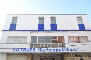 Un hotel llamado "HOTELES Metropolitan" con fachada blanca y detalles azules, que cuenta con múltiples ventanas y una entrada visible.
