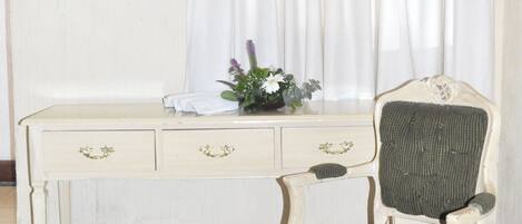 A room with a television mounted on the wall, a desk with drawers, a chair, and a curtain.
