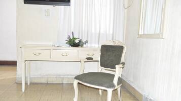 A room with a white desk, a chair, a TV mounted on the wall, and a window with curtains.
