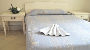 A neatly made bed with a folded towel, a small bedside table with a flower arrangement, and a drawer.