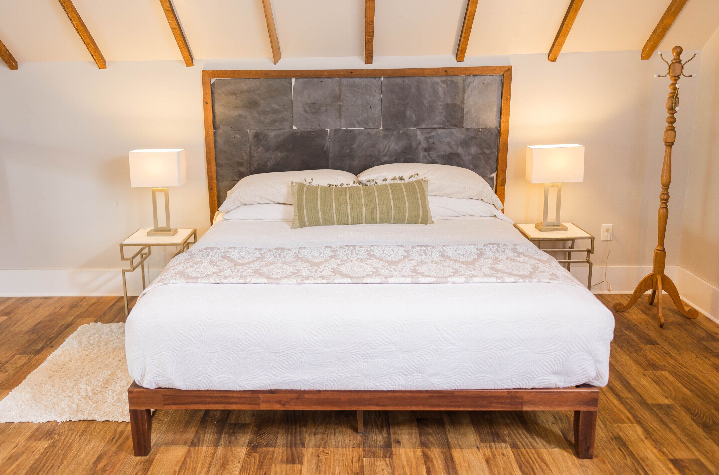 A bedroom with a wooden bed, two bedside tables with lamps, a large stone headboard, and a wooden floor.