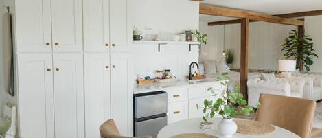 A modern kitchen with white cabinets, a built-in oven, and a dining area with a round table and chairs.