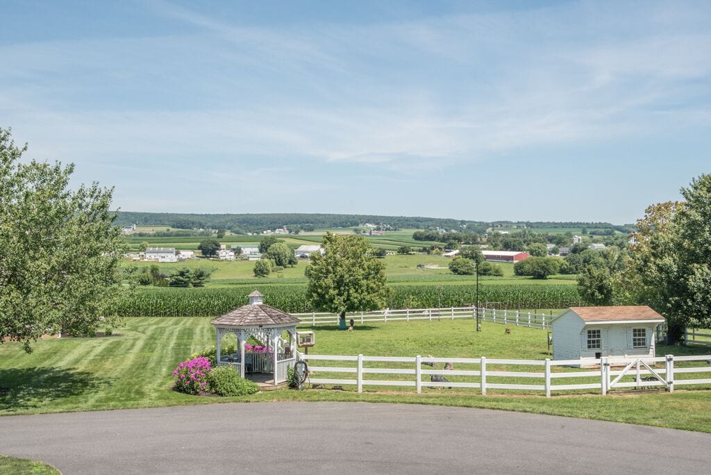 A rural landscape with a gazebo, a white fence, and a small building.