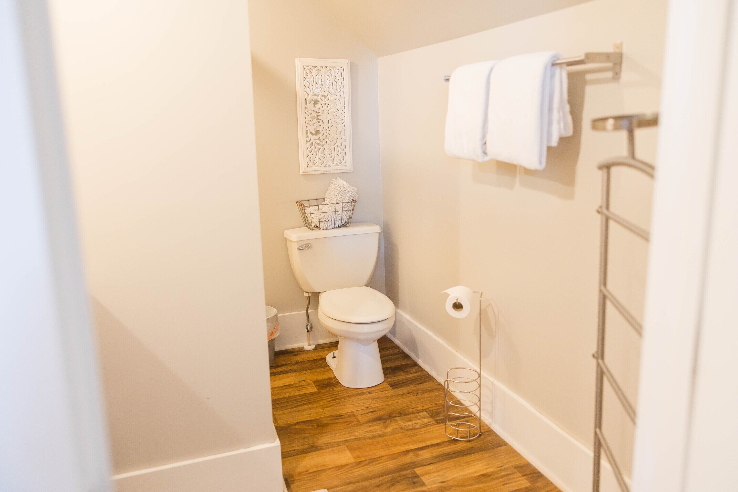 A small, clean bathroom with a white toilet, a wooden floor, a decorative wall piece, and a towel rack.
