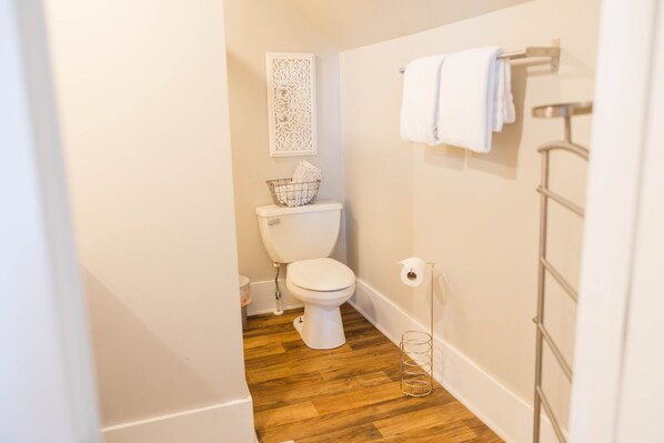 Un baño pequeño y limpio con inodoro blanco, suelo de madera, un adorno en la pared y un perchero para toallas.