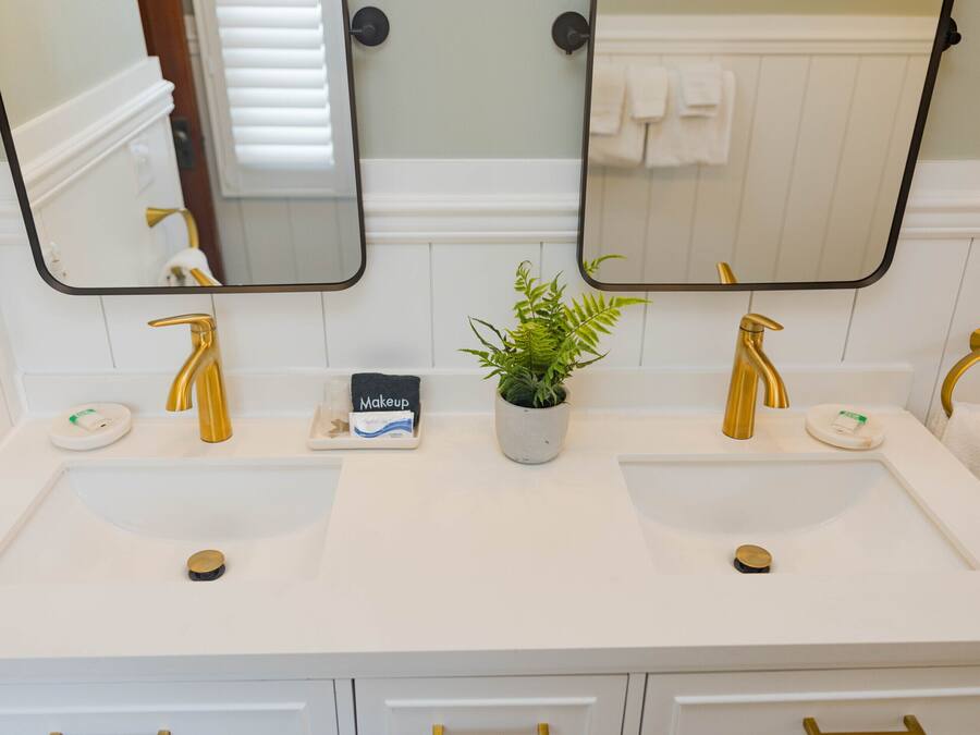 Une salle de bain avec deux lavabos, chacun doté d’un robinet doré, d’une plante en pot et d’un coin dédié au maquillage.