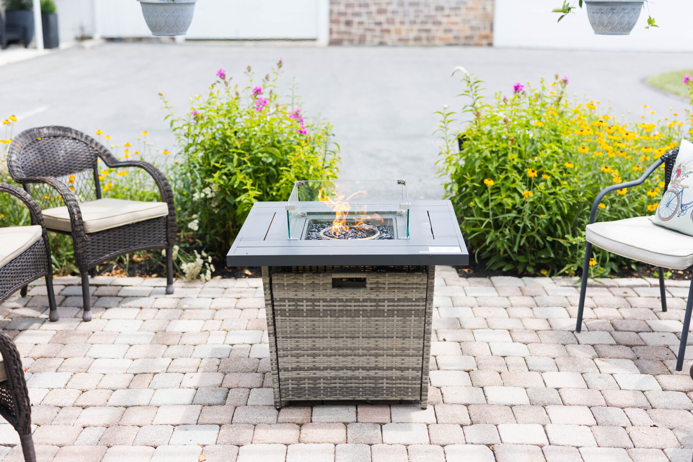 A glass-top outdoor fire feature with wicker seating on a paved patio.