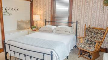 A neatly arranged bedroom with a bed, a chair, a nightstand, and a mirror.