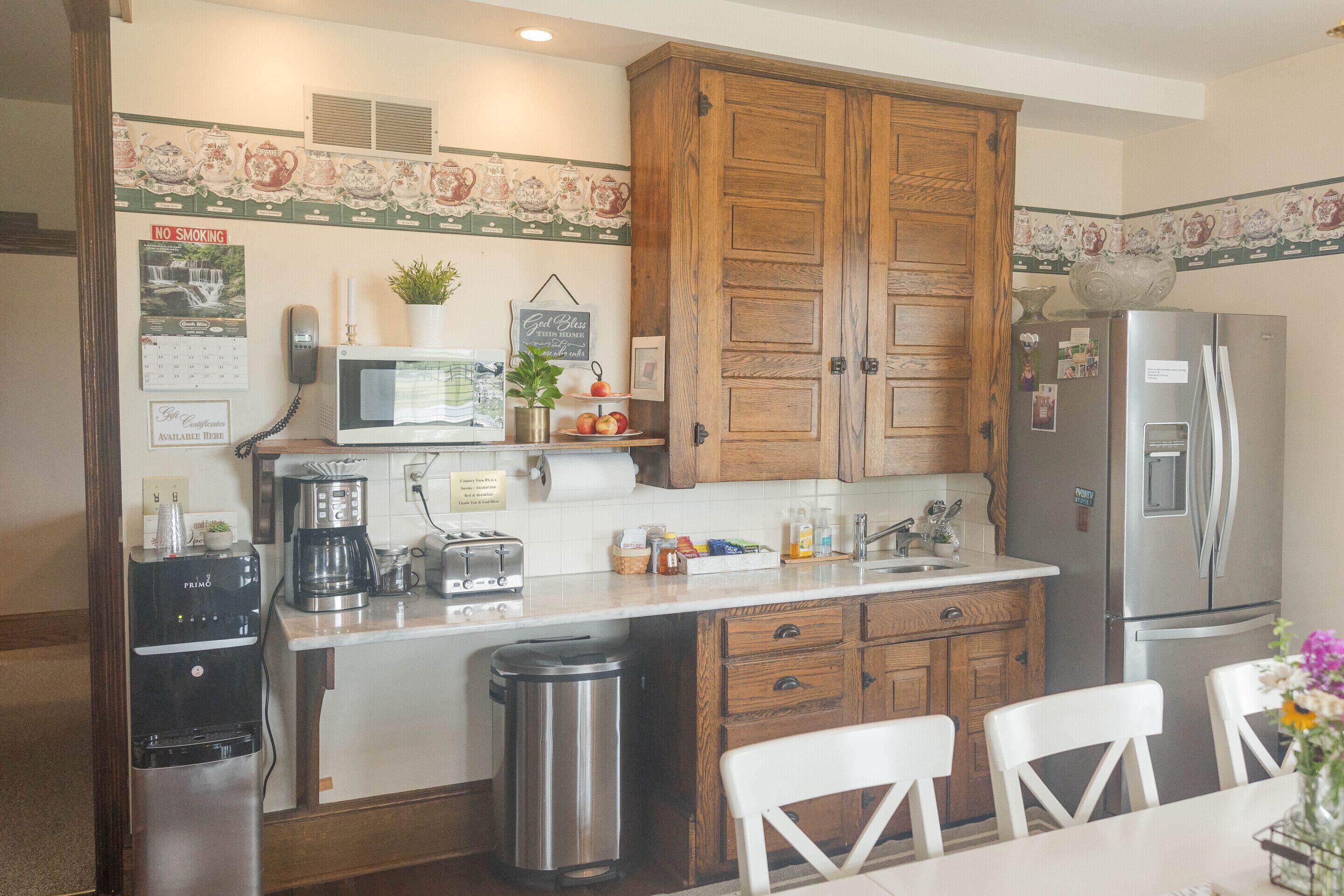 A kitchen with wooden cabinets, a refrigerator, a microwave, a coffee maker, and a trash can.