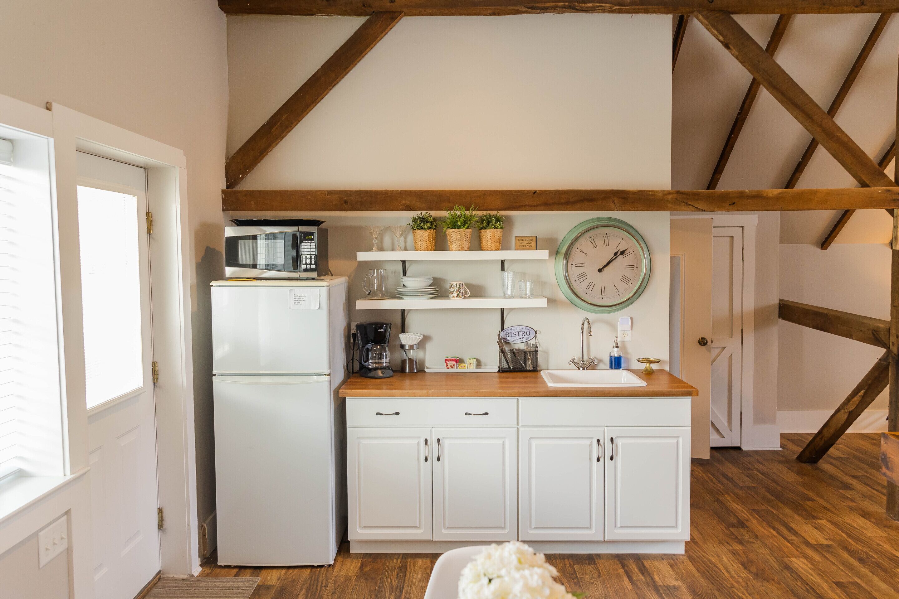 A compact kitchen with white cabinets, a wooden countertop, a white refrigerator, a clock, and a window with blinds.