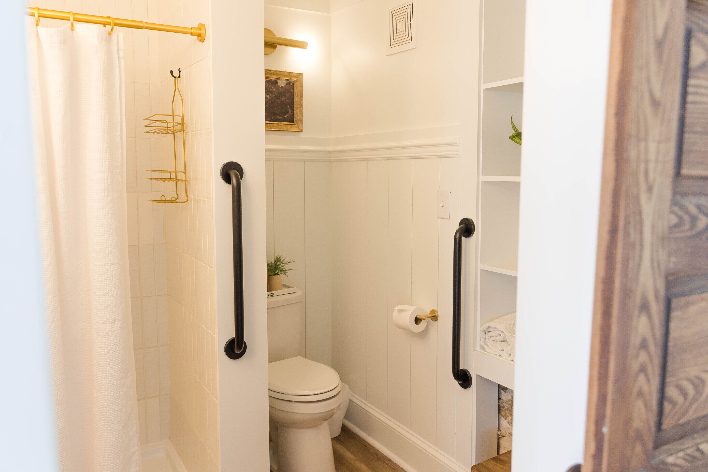 A bathroom with a white toilet, a shower curtain, a towel rack, and a shelf with a plant.