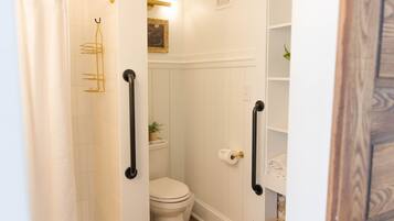 A bathroom with a white toilet, a shower curtain, a towel rack, and a shelf with a plant.