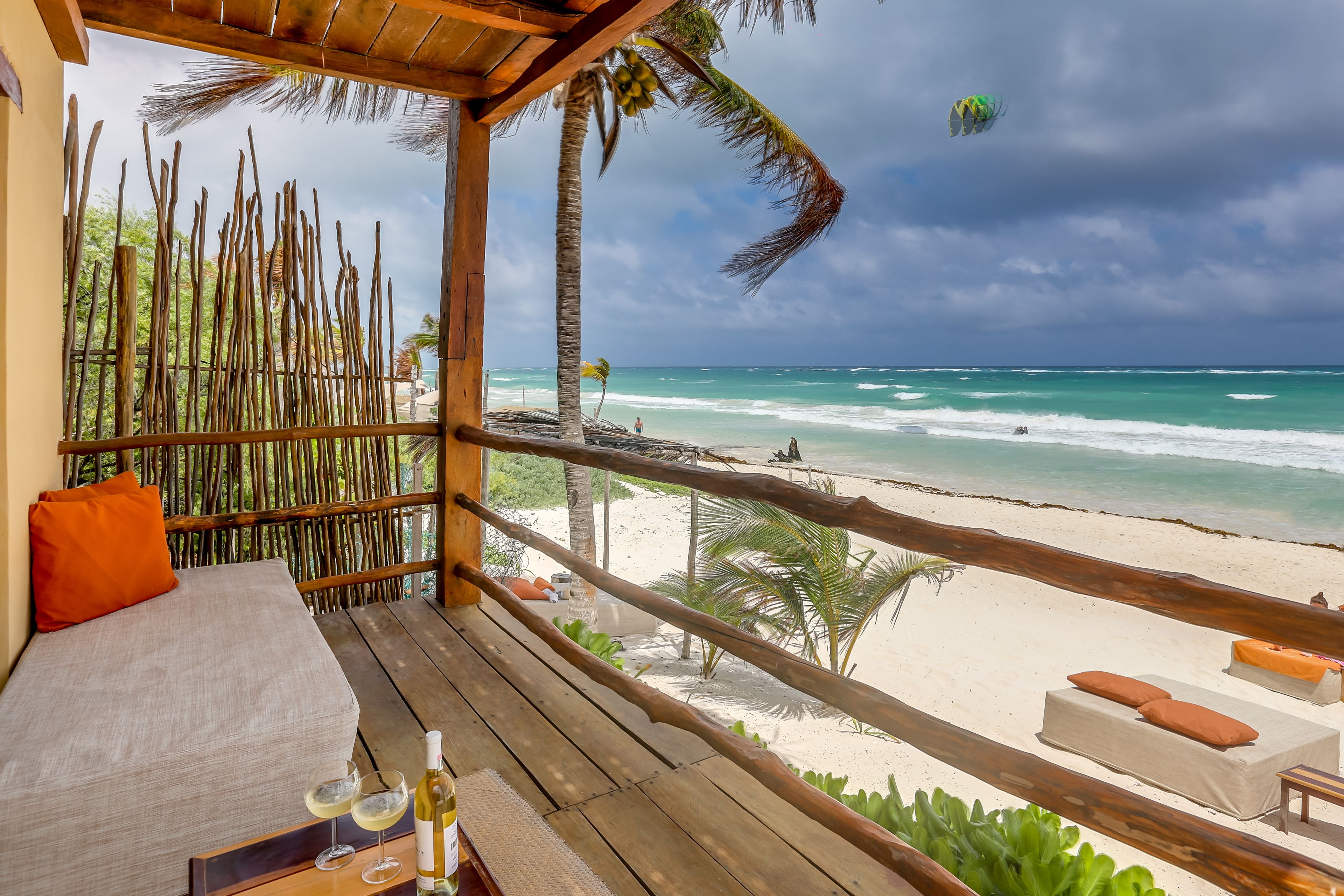 Una terraza de madera con una cama y sillones de descanso frente a una playa.