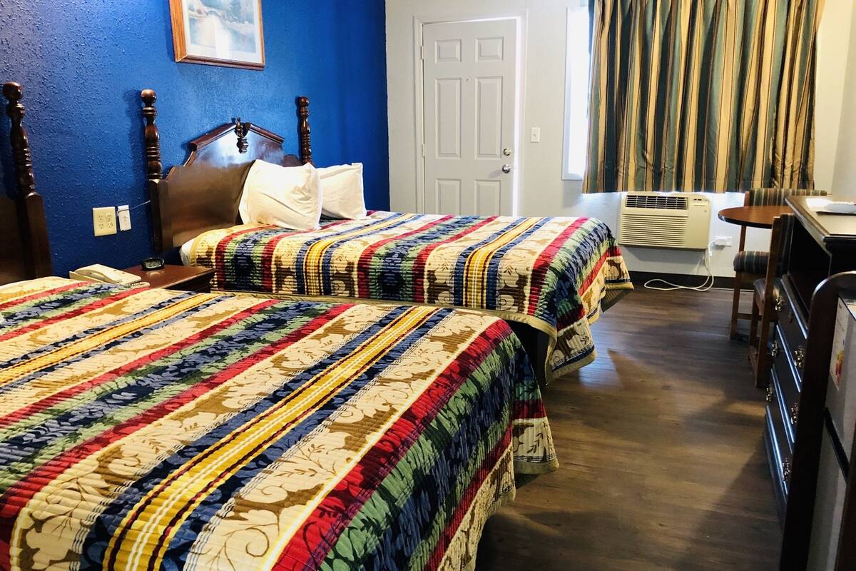 A hotel room with two beds, a desk, and an air conditioning unit.