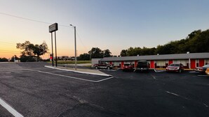 Un motel con una hilera de habitaciones, un estacionamiento y un cielo despejado.