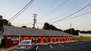 Un motel con una hilera de habitaciones, un estacionamiento y un coche estacionado al frente.